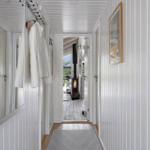 Hallway with white walls, mirror, and robe. Passage to living area with fireplace.