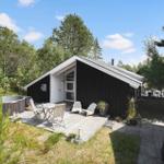 Black wooden house with terrace, hot tub, and grill area in the woods.