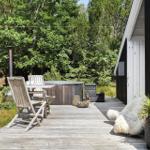 Deck with wooden table, chairs, and hot tub. Black wall and green trees in background.
