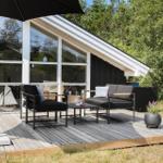 Deck with seating, umbrella, and plants in front of a house with large windows.