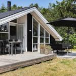 Modern wooden cabin with large balcony and outdoor seating area under umbrella.