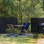 Outdoor area with table, four chairs, plants, and grill on grass.