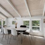 Dining area with white table and chairs, large windows, and wooden ceiling.