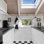 Kitchen with white cabinets, black countertops, and skylight. Black tiled floor and window with view of greenery.