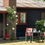 Outdoor area with table and chairs in front of a black wooden house with red window frames.