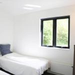 Schlafzimmer mit Bett, Fenster und Metallregal mit Körben.