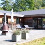 Terrasse mit Holzbank, Tisch und Pflanzen vor einem Holzhaus mit Glasfront.
