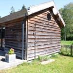 Holzterrasse mit Sitzbank, Tisch und Getränken. Hintergrund: Holzwand und Bäume.
