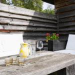 Terrasse mit Holzmöbeln, Tisch und Sitzgelegenheiten. Hintergrund: Holzwand und Bäume.