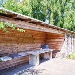 Holzhaus mit Garten, umgeben von Bäumen und Sträuchern unter blauem Himmel.