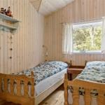 Two single beds with wooden frames, wall shelf, and window with view of forest.
