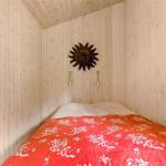 Bedroom with wood paneling, bed with red floral patterned bedspread, and sun artwork on the wall.