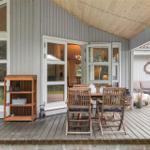 Deck with wooden table, chairs, and shelf. Entrance to apartment. Background: garden area.