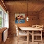 Holzhaus mit weißen Fenstern und Tür, umgeben von Grünfläche und Bäumen.