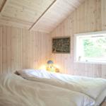 Schlafzimmer mit Holzwand, Bett und Fenster. Nachttisch mit Lampe und Bild.