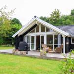 Ein Haus mit großem Balkon, Grill und Gartenmöbeln. Umgeben von Bäumen und Gras.