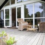 Holzterrasse mit Bänke, Pflanzen und Fenster an schwarzem Haus
