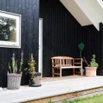 Terrasse mit Tisch und Stühlen, hängenden Körben und dunklem Holzhaus.