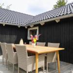 Terrasse mit Rattanmöbeln, Holztisch und Pflanzenkörben. Hintergrund: Haus mit großen Fenstern.