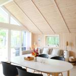 Wohnzimmer mit Sofa, Tisch und Fenster. Holzwände und -decke. Bilder und Pflanzen.