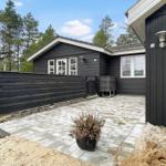 Backyard with black fence, garden table and grill area. Stone-paved path and trees in the background.