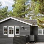 Outdoor area with table and two chairs next to a black wooden house in the woods.