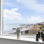 Gelbes Haus mit rotem Dach auf grünem Grundstück mit Blick aufs Meer.