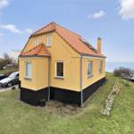 Gelbes Haus mit rotem Dach und Fenstern, umgeben von Gras und Bäumen.