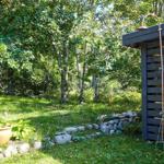 White garden table and chairs near woodpile and trees.