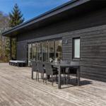 Moderne Holzhütte mit Terrasse, Grill und Sitzgelegenheiten. Umgeben von Wald.