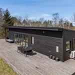 Terrasse mit Tisch und Stühlen vor einem dunklen Holzhaus mit Glasfront.