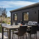 Terrasse mit Tisch und Stühlen vor einem Holzhaus mit Glasfront.