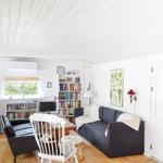 Wohnzimmer mit Sofa, Bücherregal und Holztisch. Fenster, Decke und Boden sind sichtbar.