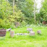 Holzgestell mit Bank und Tisch im Garten. Umgeben von Grün und Steinen.