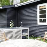 Schwarze Holzwand neben grünem Garten mit zwei Stühlen und dekorativen Käfigen.