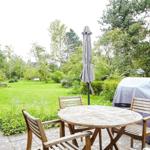 Zwei hölzerne Liegestühle und ein Tisch stehen im grünen Garten unter Bäumen.