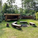 Holzterrasse mit Grill, Sitzbänken und Hängematte im Grünen.