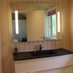 Bad mit Dusche, Waschbecken und Spiegel. Holzwände und Toilettenpapierhalter sichtbar.