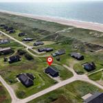 Haus mit rotem Markierungspunkt in Strandnähe, umgeben von Grünflächen und weiteren Häusern.
