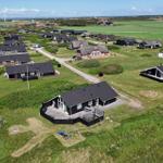 Aerial view of holiday homes with grassy terrain and wind turbines in the distance.