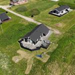Haus mit Holzterrasse, Whirlpool und Spielplatz auf grünem Grundstück.