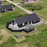 Schwarzes Haus mit Terrasse, Grillplatz und Spielplatz auf grünem Grundstück.
