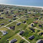 Aerial view of a coastal village with houses, greenery, and a sandy beach.