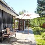 Schwarzes Holzhaus mit Dach und Terrasse umgeben von Bäumen und Gras.