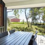 Terrasse mit Grill, Liegestühlen und Tisch. Holzwand und Blick auf Bäume.