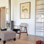 Wohnzimmer mit Ecksofa, Holztisch und Wandbildern. Decke mit Holzverkleidung und großes Fenster.