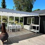 Terrasse mit Holzdecke, Grill und Garten. Hintergrund: Rasen und Hecke.