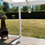 Ein Haus mit Terrasse, Garten und Bäumen unter blauem Himmel.