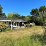 Ein Haus mit Terrasse, Garten und Bäumen unter blauem Himmel.