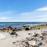 Strand mit Kies und Steinen, Meer und klarer blauer Himmel.